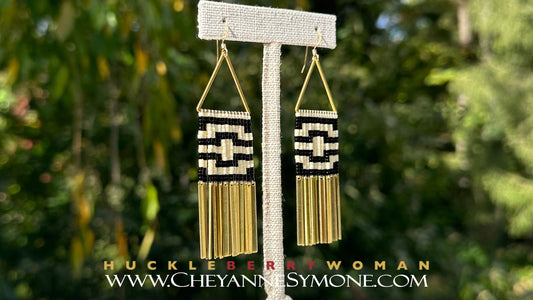 3 inch dangle fringe style beaded earrings featuring an ivory and black geometric raven pattern hanging from gold-filled earring wires, brass triangles and long brass jingles. 